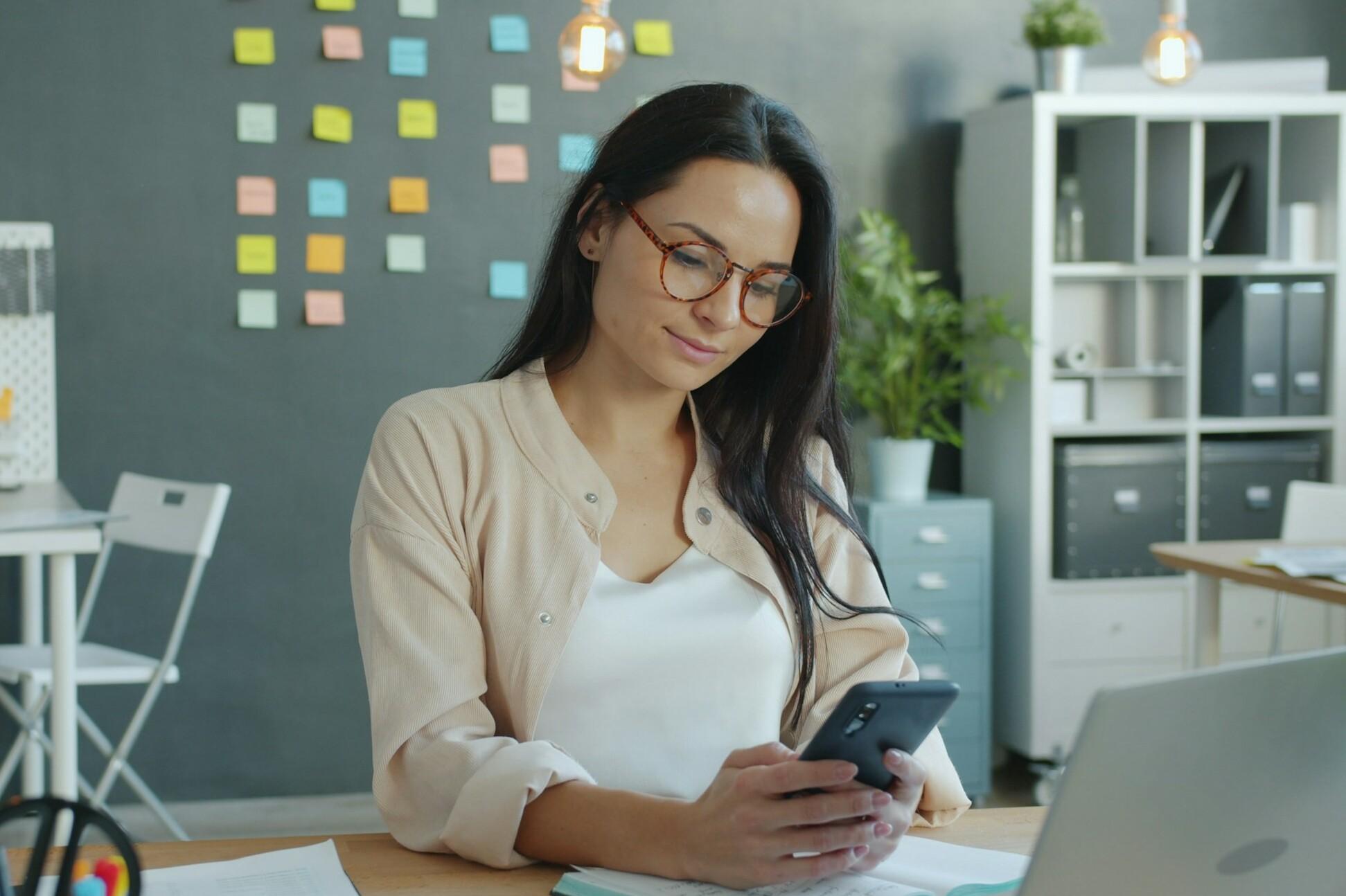 Frau im Büro Eine Frau am Schreibtisch sieht auf ihr Handy