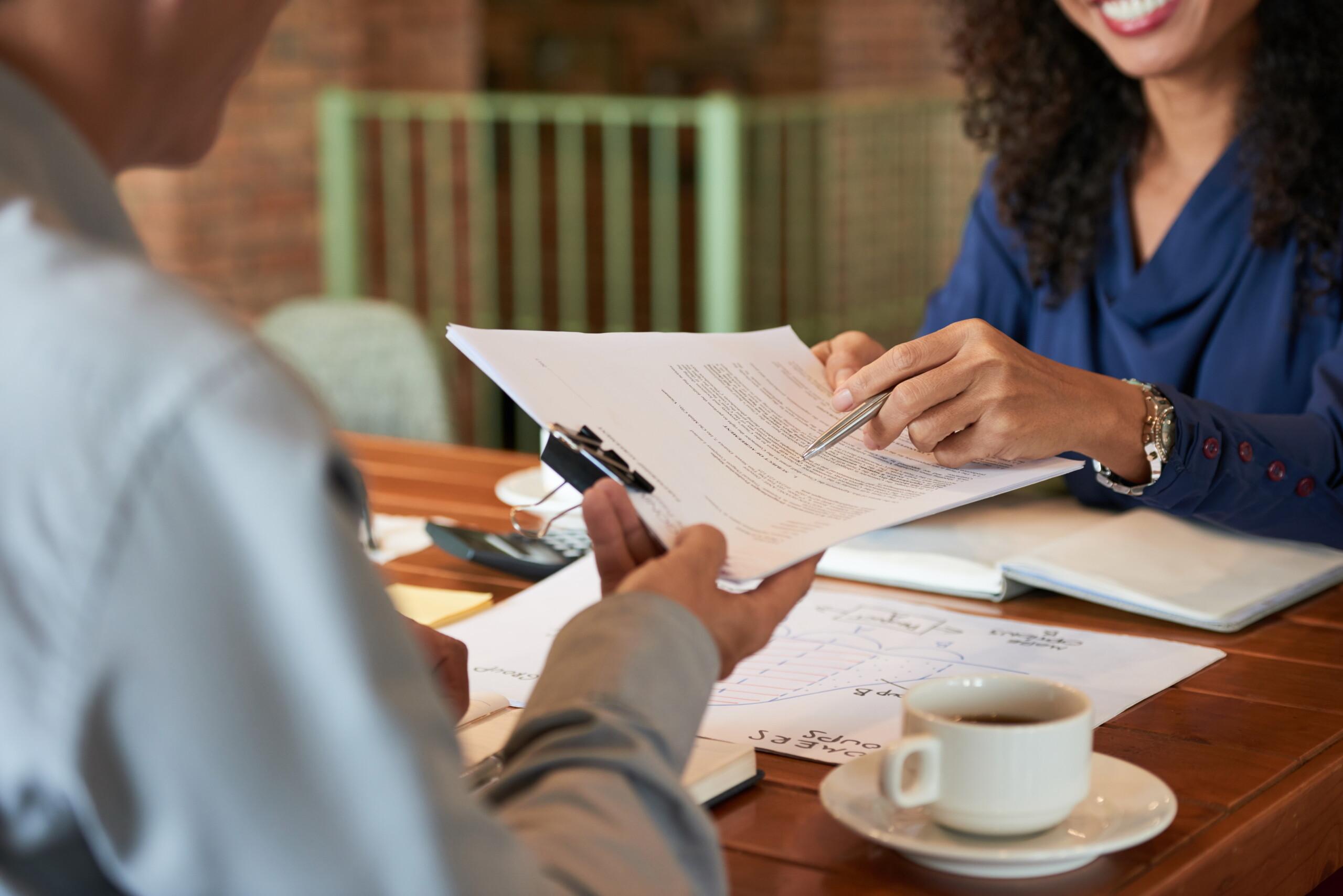 Two people sit at a desk and one shows the other a place on a document