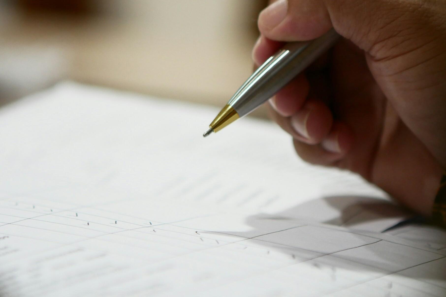 Stift Eine Hand mit einem Stift in der Hand ist über einem Blatt Papier und scheint etwas abzuhaken.