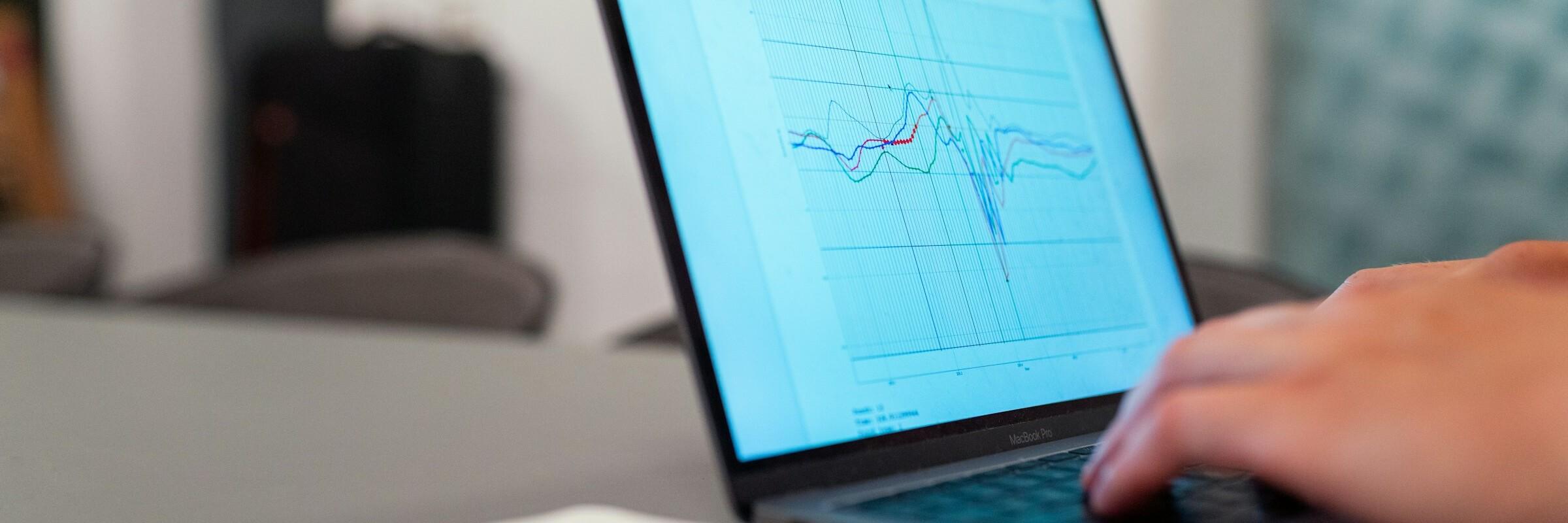 Person, die einen schwarzen Laptop benutzt Hände tippen auf einem Laptop, der Verlaufskurven in einem Diagramm zeigt