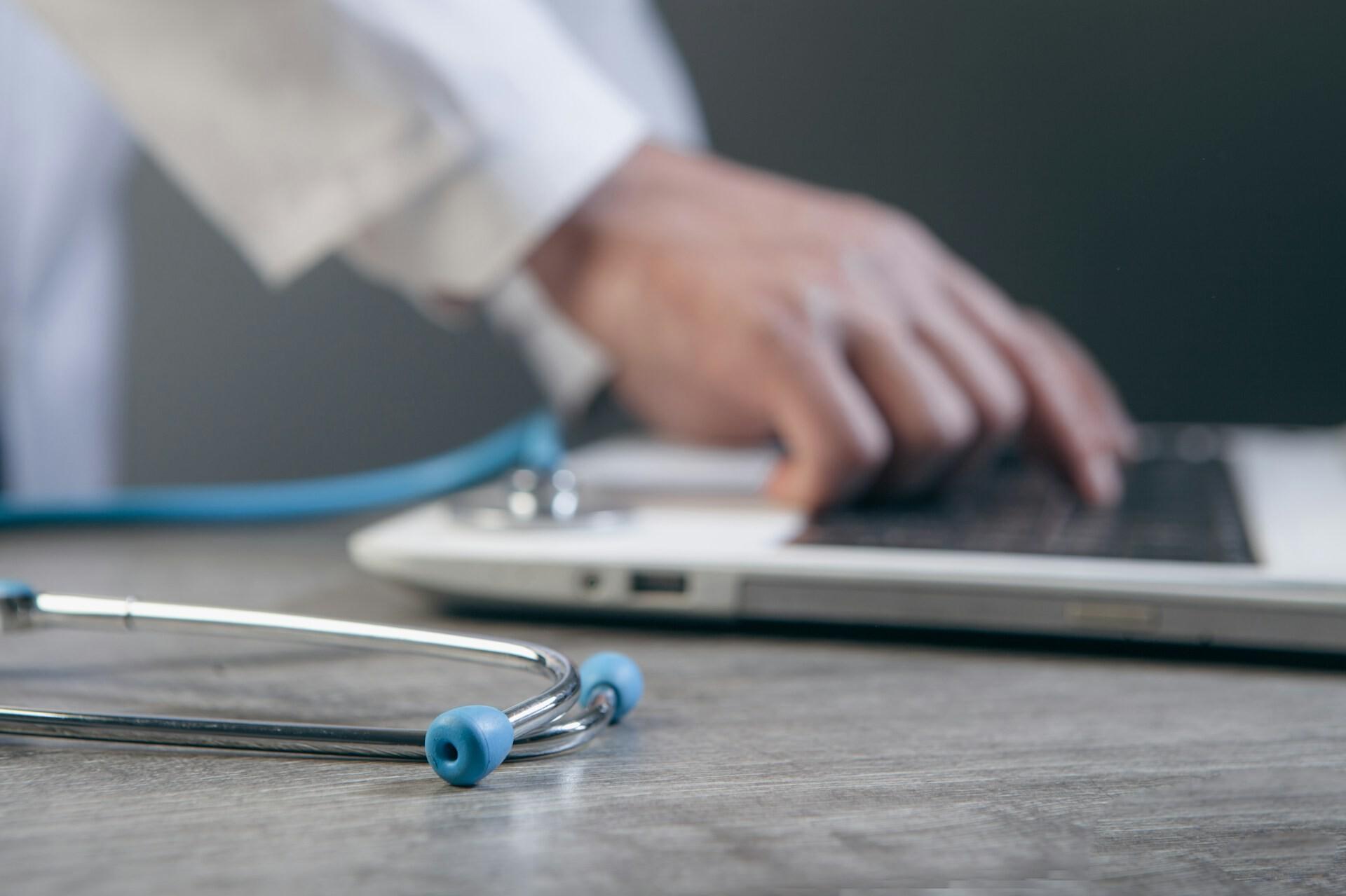 Arzt tippt auf Laptop Die Hände einer Person tippen auf einem Laptop, davor liegt ein Stethoskop