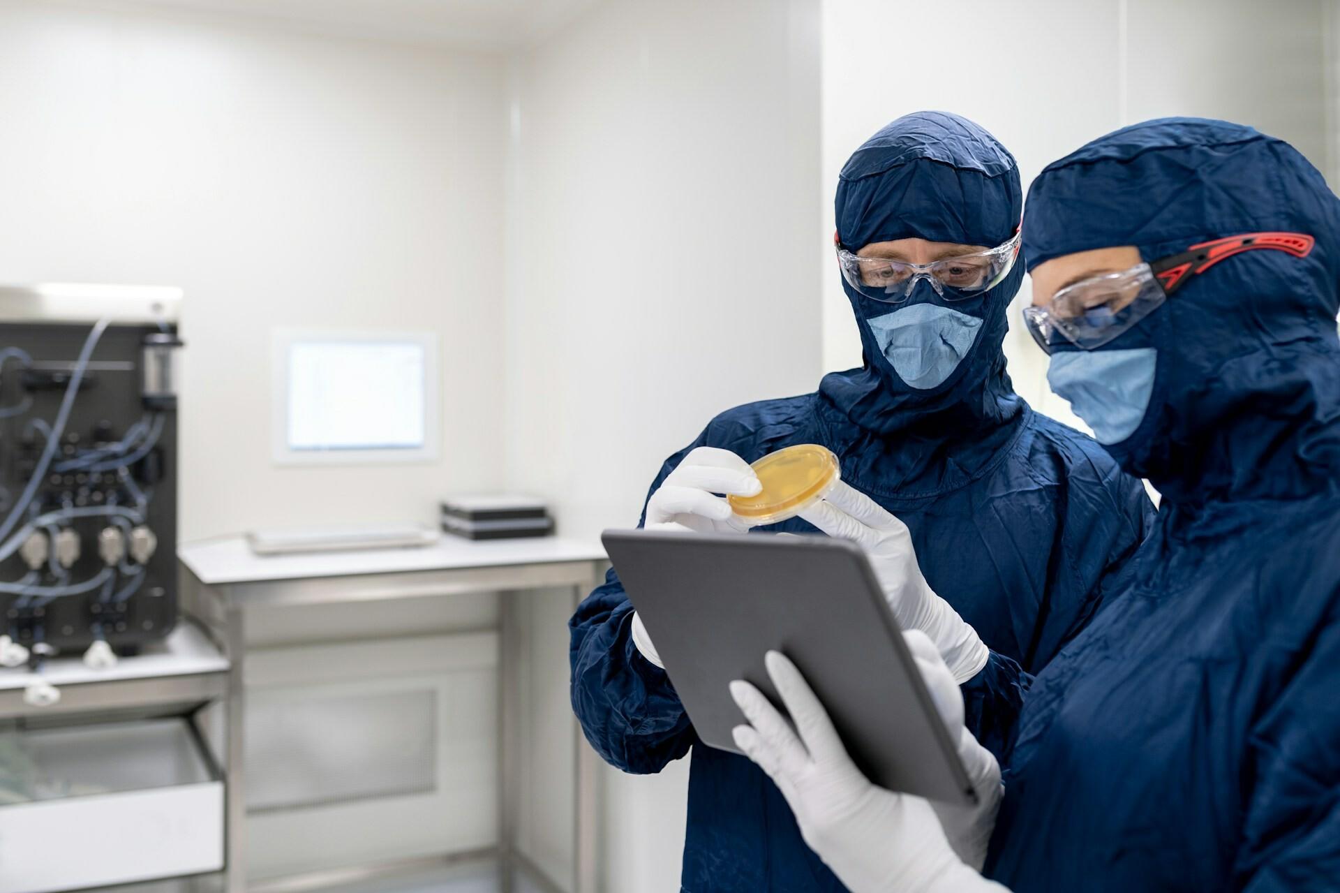 Labor Zwei Personen im Schutzanzug prüfen gemeinsam eine Probe durch Blick in ein Tablet