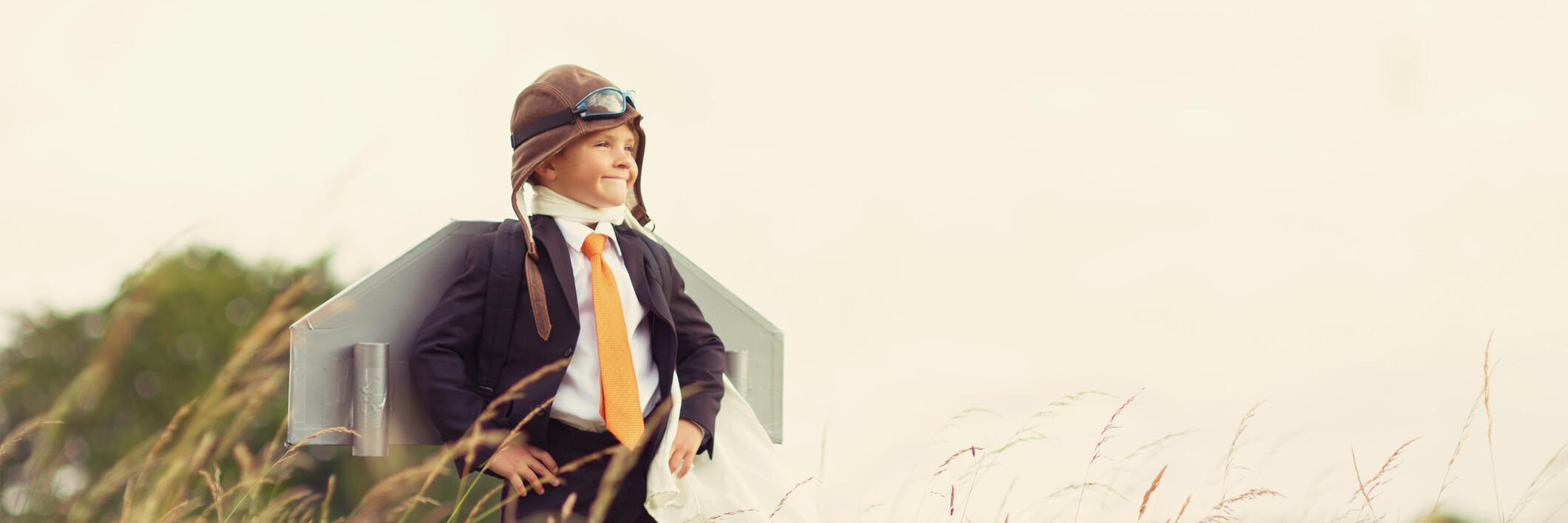 Junge mit Helm und Umhang in Superhelden-Pose