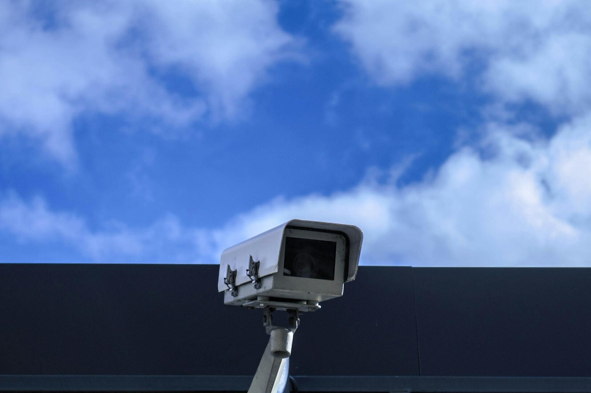 Überwachungskamera Überwachungskamera vor einem Gebäude, darüber blauer Himmel mit Wolken