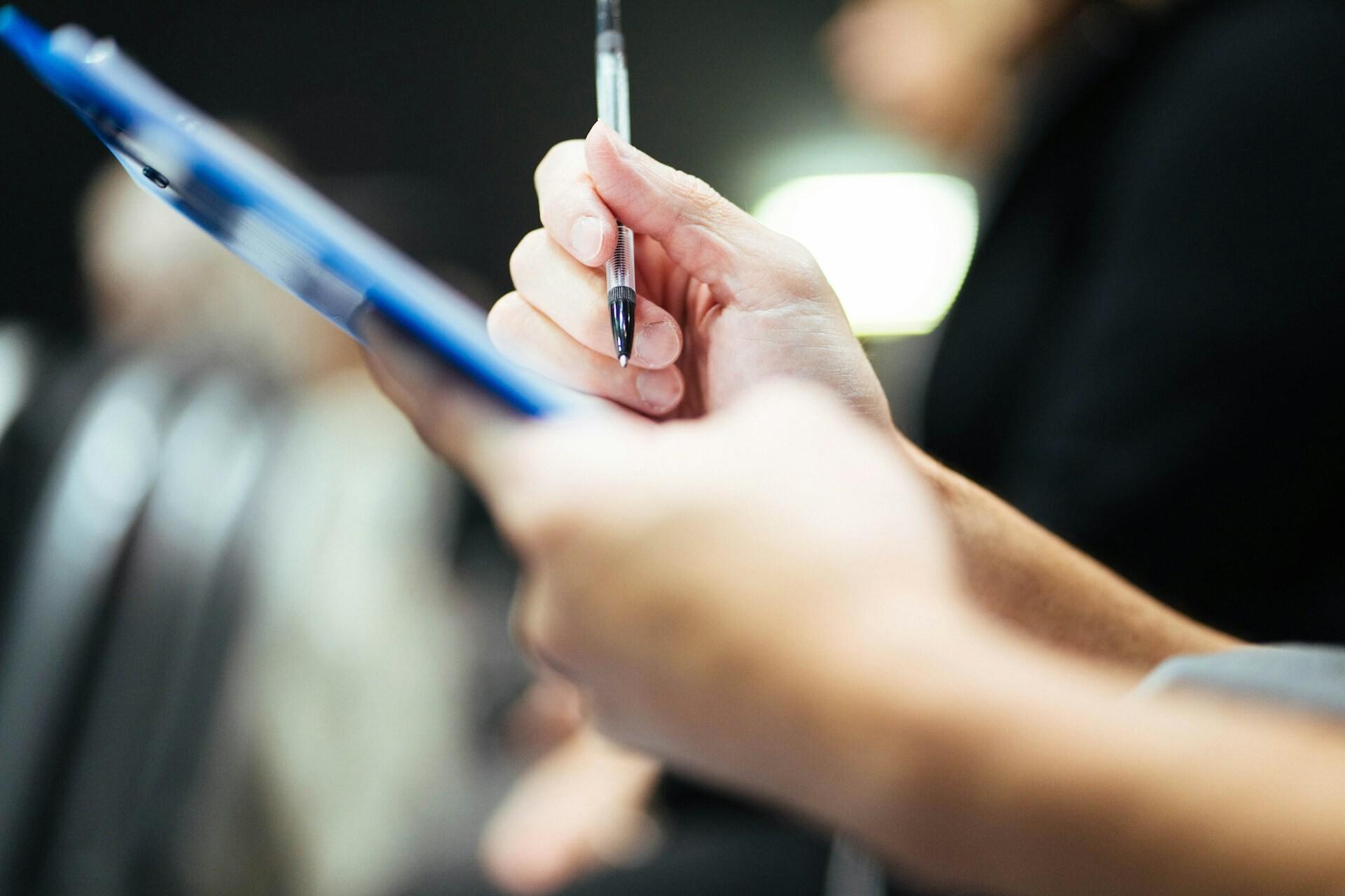 Dokumentation Zwei Hände einer Person halten ein Klemmbrett und einen Stift in der Hand